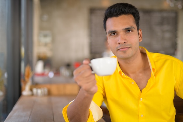 Joven indio guapo tomando café junto a la ventana en el c