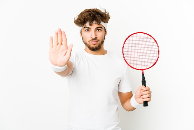 Joven indio jugando bádminton de pie con la mano extendida mostrando la señal de stop, impidiéndote.