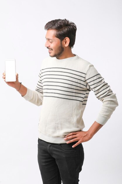 Joven indio que muestra la pantalla del teléfono inteligente con fondo blanco.