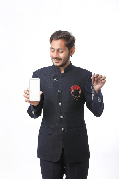 Joven indio en ropa tradicional y mostrando la pantalla del teléfono inteligente sobre fondo blanco.
