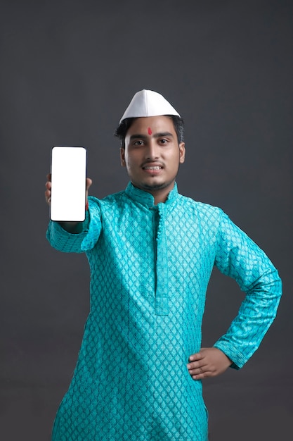 Joven indio en ropa tradicional y mostrando smartphone.