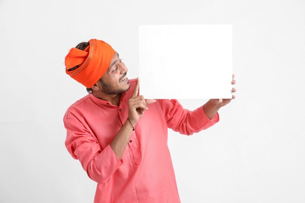 Joven indio sosteniendo el tablero de cartón blanco en la pared blanca