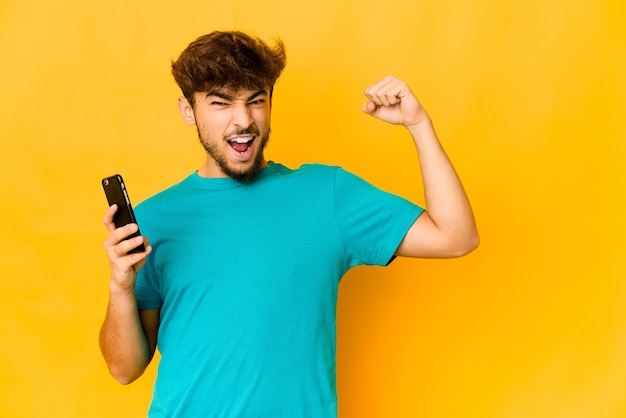 Joven indio sosteniendo un teléfono levantando el puño después de una victoria, concepto ganador.