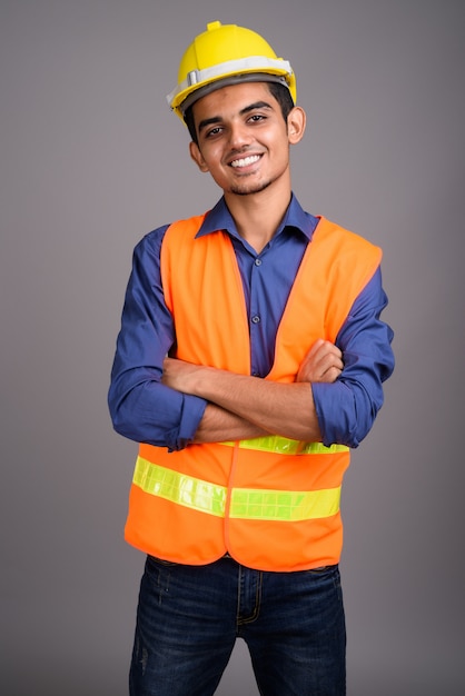 Joven indio trabajador de la construcción contra la pared gris