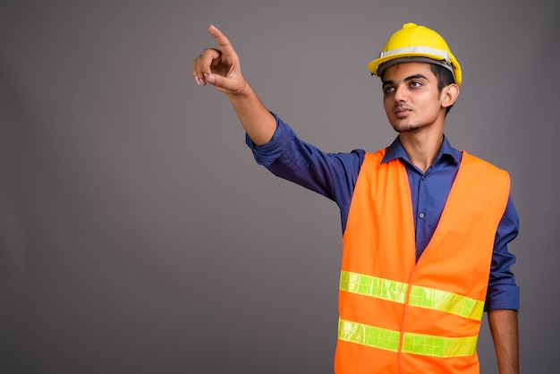 Joven indio trabajador de la construcción contra la pared gris