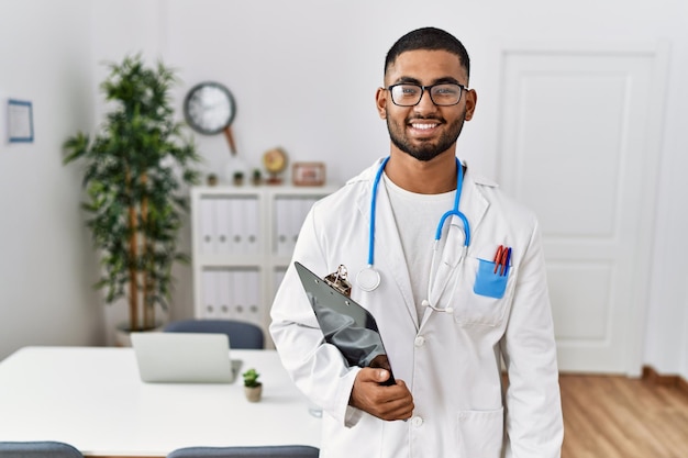 Joven indio con uniforme médico y estetoscopio con una sonrisa feliz y fresca en la cara de una persona afortunada