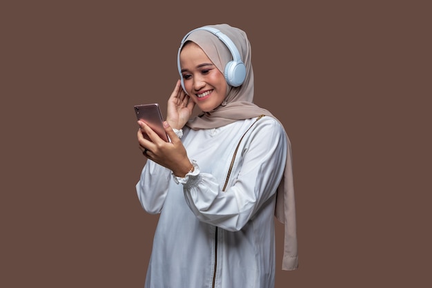 Joven indonesia en hijab escuchando música con auriculares inalámbricos mientras cierra los ojos