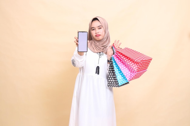 una joven indonesia musulmana que usa un hijab tiene miedo de fruncir el ceño mostrando una pantalla de teléfono celular y un coche