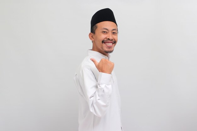 Un joven indonesio confiado apuntando a un lado al espacio de copia con el pulgar aislado en fondo blanco