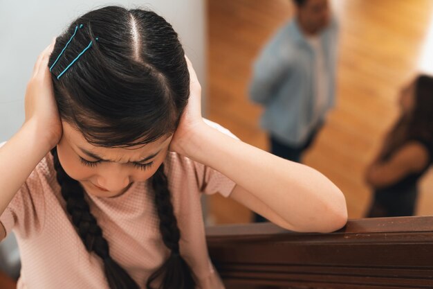 Una joven infeliz mira a sus padres discutiendo desde la escalera.