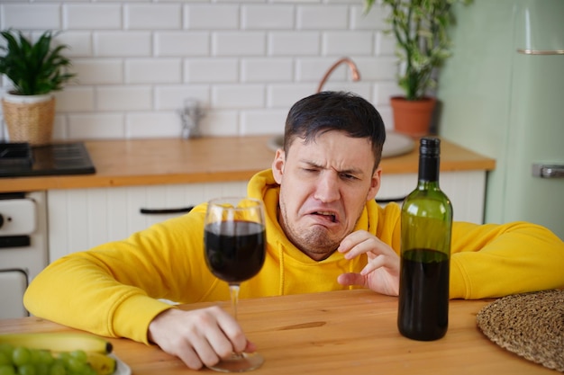 Un joven infeliz tiene dolor de cabeza por el vino tinto Un hombre adulto se siente mal por el alcohol mientras está en la cocina