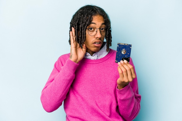 Joven informático afroamericano aislado de fondo azul tratando de escuchar un chisme