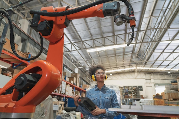 Joven ingeniera afroamericana operando máquina de brazo robot de soldadura en fábrica de almacén