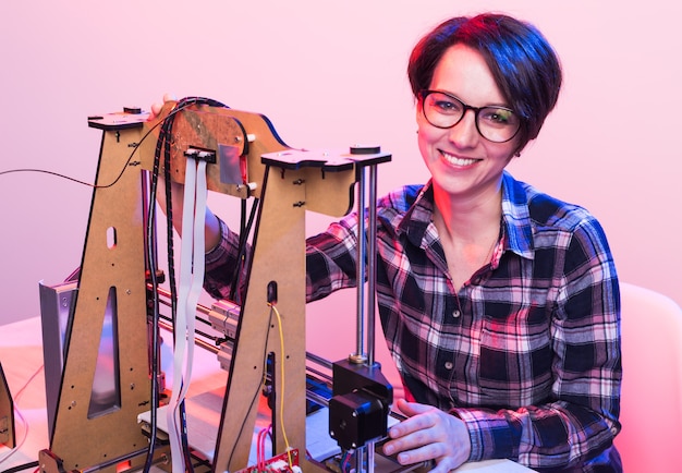 Joven ingeniera diseñadora usando una impresora en el laboratorio y estudiando un concepto de prototipo de producto, tecnología e innovación.