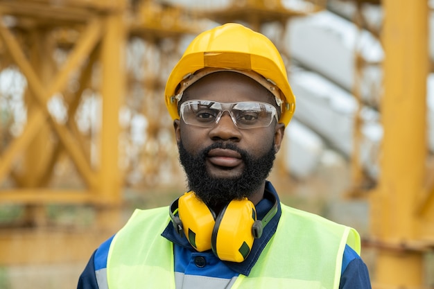 Joven ingeniero africano en ropa de trabajo y casco protector mirándote