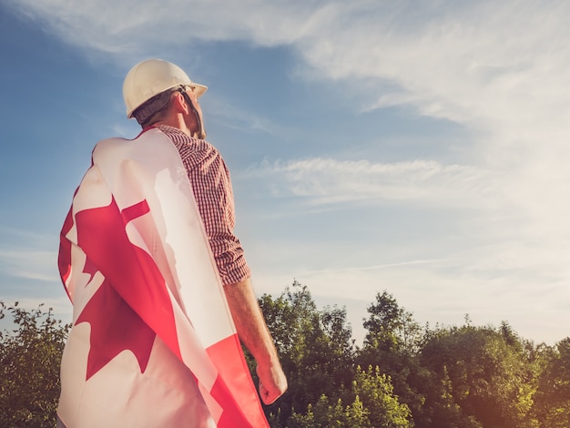 Foto joven ingeniero, casco blanco y bandera canadiense