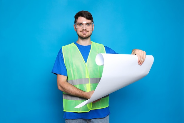 Joven ingeniero civil con planos sobre fondo azul.