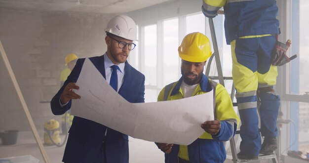 Joven ingeniero discutiendo anteproyecto con trabajador de la construcción en el sitio de construcción