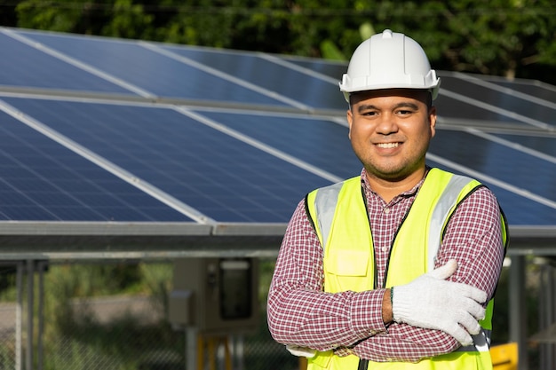 Joven ingeniero eléctrico asiático parado frente a la granja de paneles de células solares. Él revisando e instalando. Concepto de energía del generador solar.