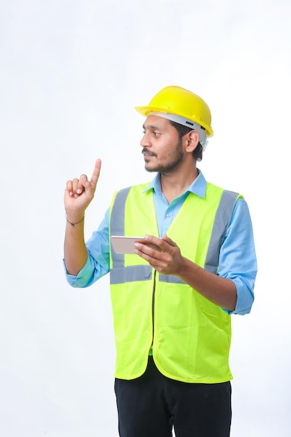 Joven ingeniero indio con casco y smartphone con fondo blanco.