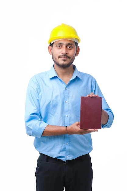 Joven ingeniero indio o estudiante que usa casco y muestra un diario sobre fondo blanco.