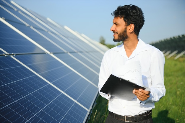 Joven ingeniero con tableta en la mano de pie cerca de paneles solares agricultura tierra de granja con fondo azul claro energía renovable energía limpia