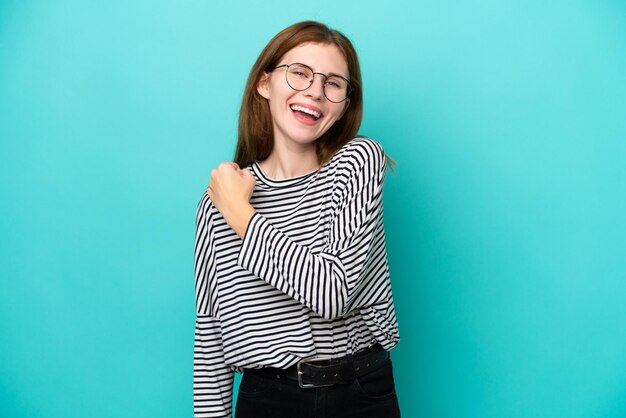 Joven inglesa aislada de fondo azul celebrando una victoria