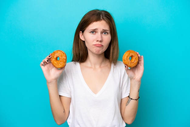 Joven inglesa aislada de fondo azul sosteniendo donuts con expresión triste