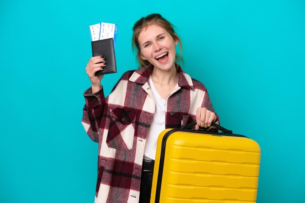 Joven inglesa aislada de fondo azul en vacaciones con maleta y pasaporte