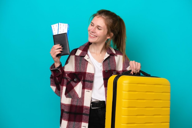 Joven inglesa aislada de fondo azul en vacaciones con maleta y pasaporte