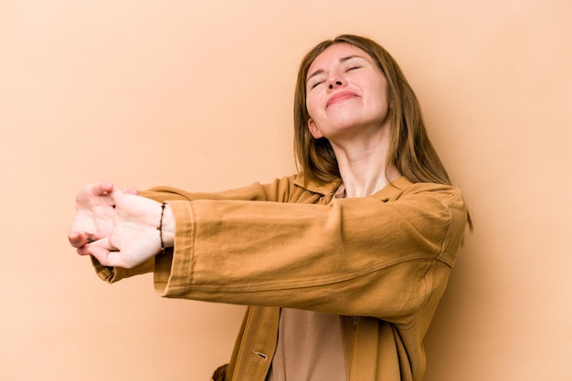 Foto joven inglesa aislada de fondo beige estirando los brazos en posición relajada