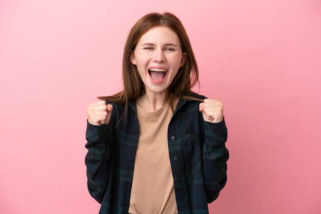 Joven inglesa aislada de fondo rosa celebrando una victoria en posición ganadora