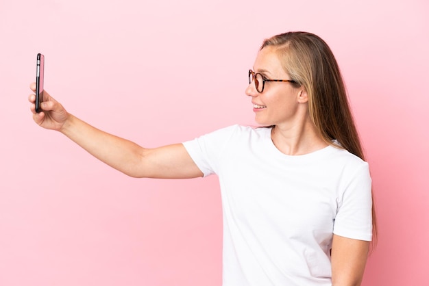 Joven inglesa aislada de fondo rosa haciendo un selfie