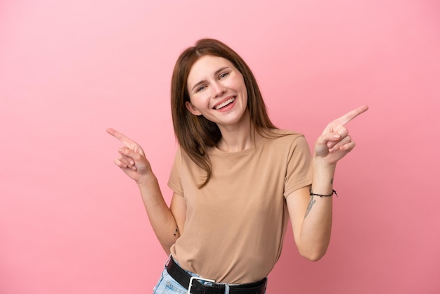 Joven inglesa aislada de fondo rosa señalando con el dedo a los laterales y feliz