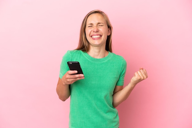 Joven inglesa aislada sobre fondo rosa con teléfono en posición de victoria