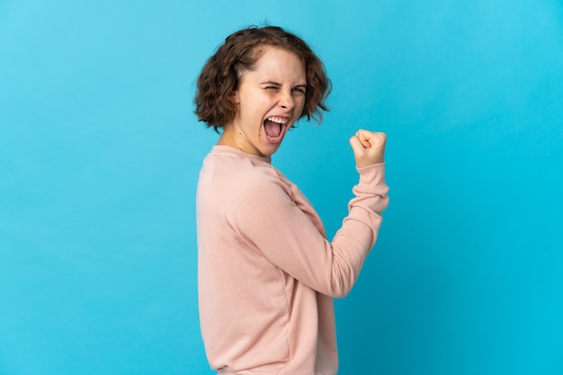 Foto joven inglesa aislada sobre pared azul celebrando una victoria