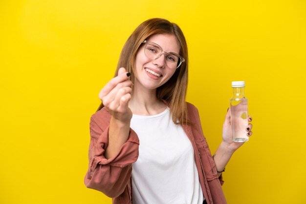 Joven inglesa con una botella de agua aislada de fondo amarillo haciendo gestos de dinero