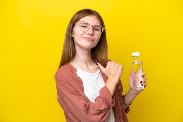 Joven inglesa con una botella de agua aislada de fondo amarillo orgullosa y satisfecha