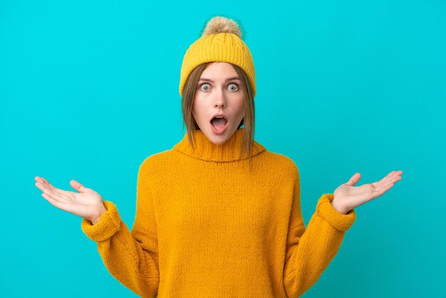 Joven inglesa con chaqueta de invierno aislada de fondo azul con expresión facial impactada