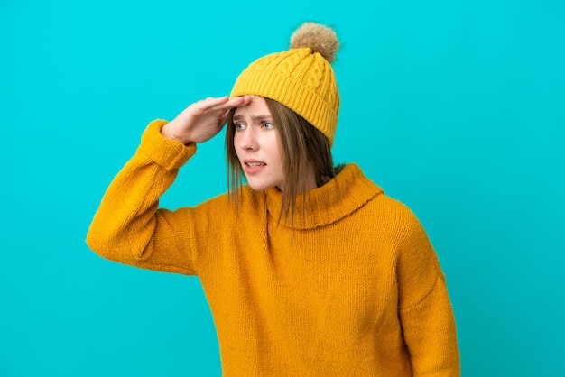 Joven inglesa con chaqueta de invierno aislada de fondo azul mirando lejos con la mano para mirar algo