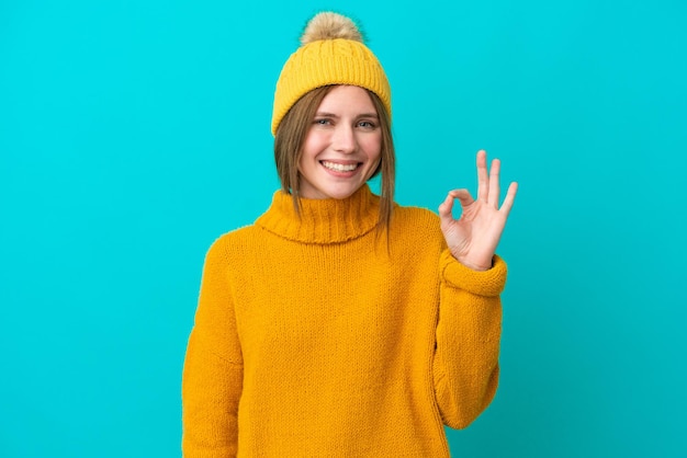 Joven inglesa con chaqueta de invierno aislada de fondo azul mostrando el signo de ok con los dedos