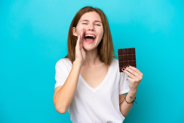 Joven inglesa con chocolat aislada de fondo azul gritando con la boca abierta