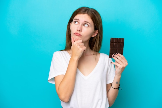 Joven inglesa con chocolat aislada de fondo azul que tiene dudas