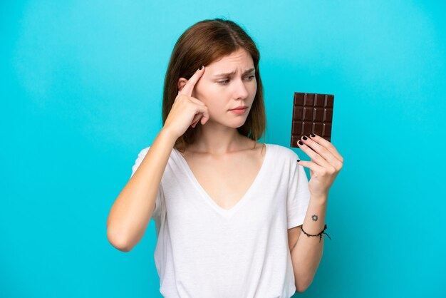 Joven inglesa con chocolate aislada de fondo azul que tiene dudas y piensa