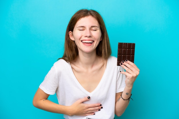 Foto joven inglesa con chocolate aislado de fondo azul sonriendo mucho