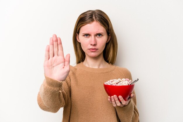 Joven inglesa comiendo cereales aislada de fondo blanco de pie con la mano extendida mostrando la señal de stop que te impide