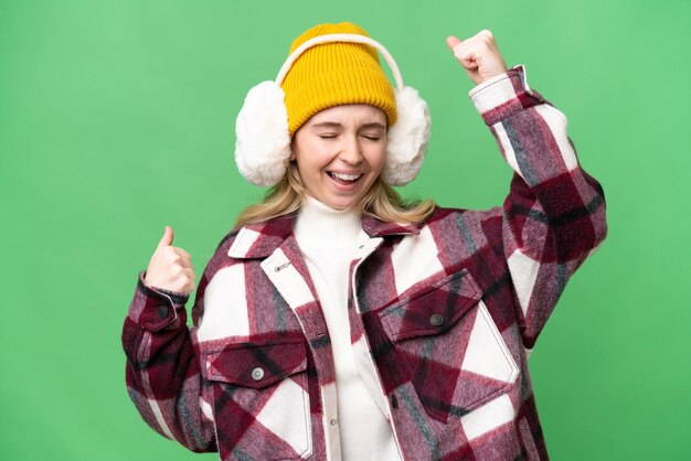 Joven inglesa con manguitos de invierno sobre un fondo aislado celebrando una victoria