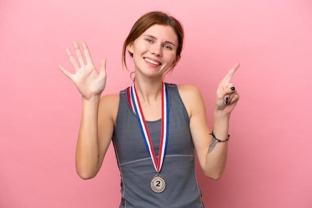 Joven inglesa con medallas aisladas de fondo rosa contando seis con los dedos