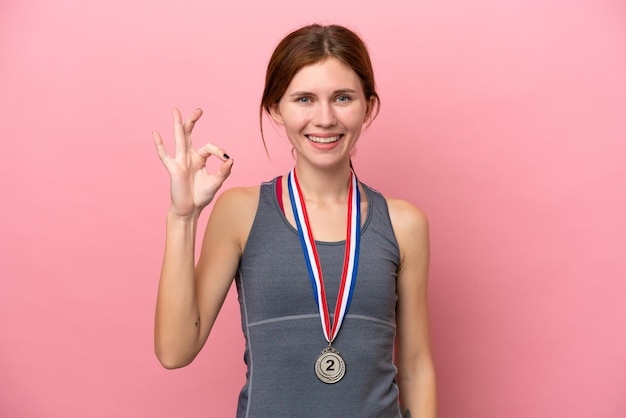 Joven inglesa con medallas aisladas en un fondo rosa mostrando el signo de ok con los dedos