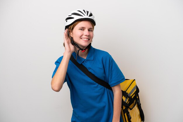 Joven inglesa con mochila térmica aislada de fondo blanco escuchando algo poniendo la mano en la oreja